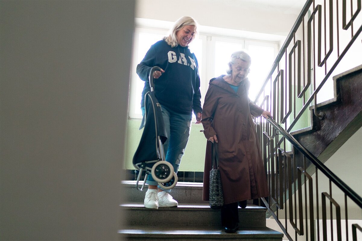 Pflegekraft begleitet Seniorin mit Rollator sicher die Treppe hinunter