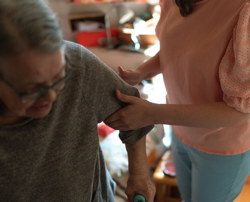 Pflegekraft hilft einer Seniorin liebevoll beim Anziehen – Unterstützung im Alltag durch den ambulanten Pflegedienst